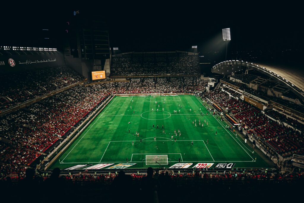 pexels-photo-31160101-31160101 High-angle view of a vibrant football match with enthusiastic fans in a large stadium at night.