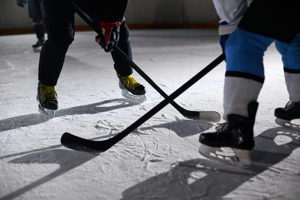 pexels-photo-6468938-6468938 Close-up of hockey players battling for puck during an intense face-off on a lighted ice rink.